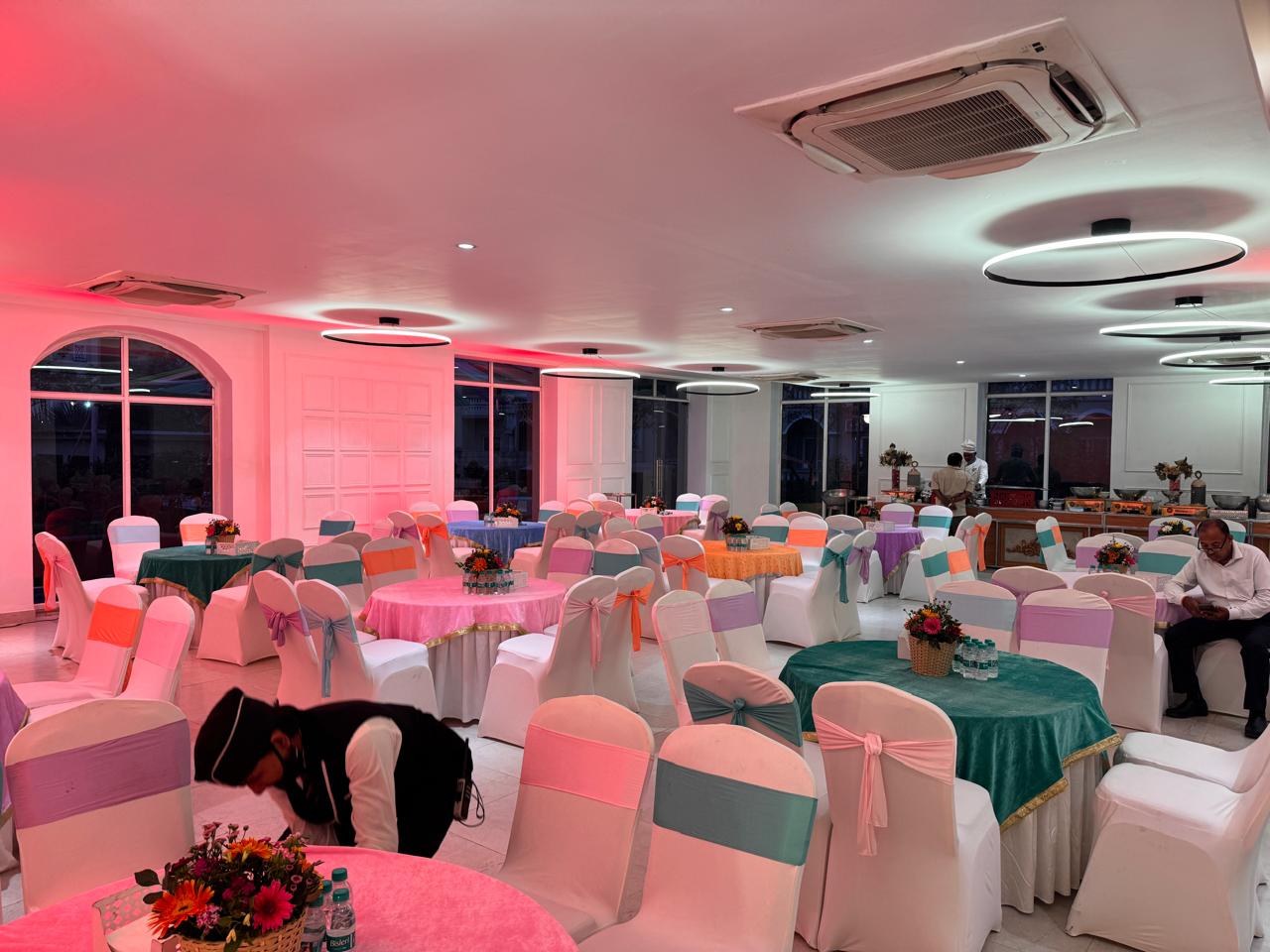 Banquet hall with pink and white lighting and floral centerpieces in Greater Noida